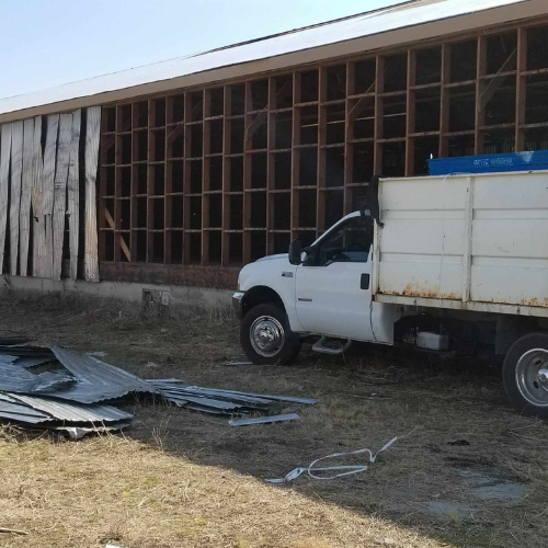 White truck parked next to a building with exposed wooden framing and debris.
