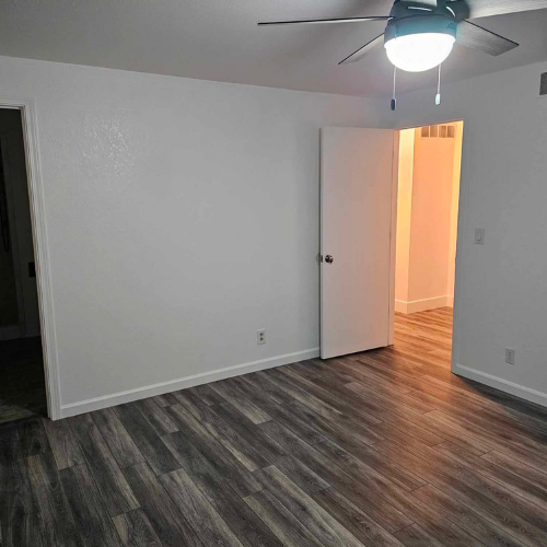 Empty room with gray wood-look flooring, white walls, and a ceiling fan. Two doorways and a light fixture are visible.