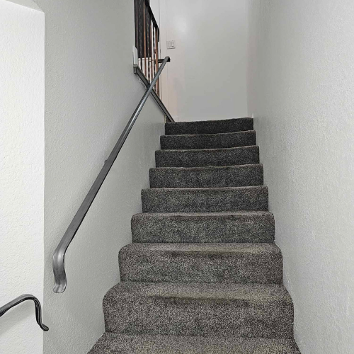 Staircase with gray carpeted steps and metal handrails against light gray walls.