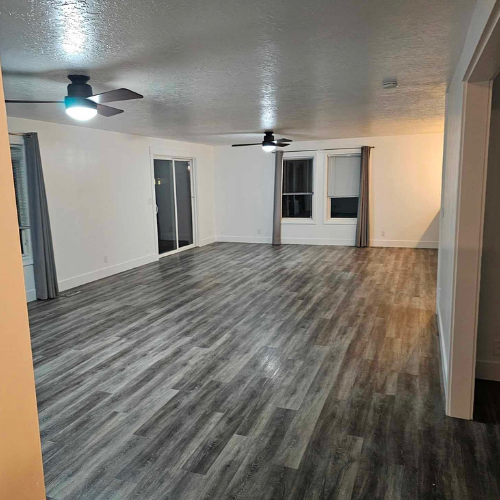 Empty room with gray wood-look flooring, white walls, and a ceiling fan. A window is in the back.
