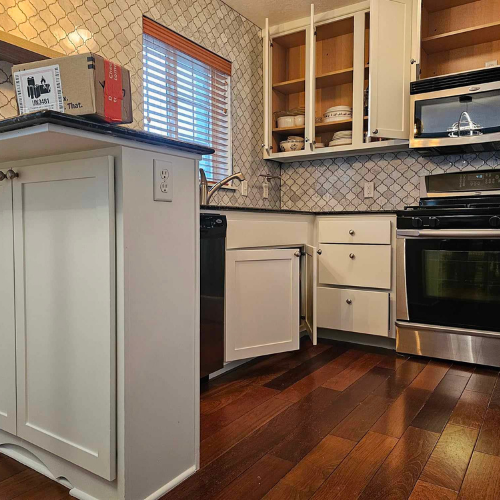 Kitchen with open cabinets, dark countertops, white cabinetry, stainless steel appliances, and dark wood floors.
