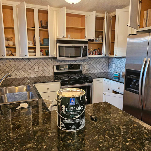 Kitchen with open white cabinets, black countertops, and a can of green paint.
