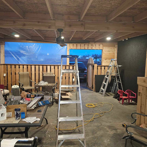 Indoor space under construction with tools, furniture, ladder, and a ceiling fan.