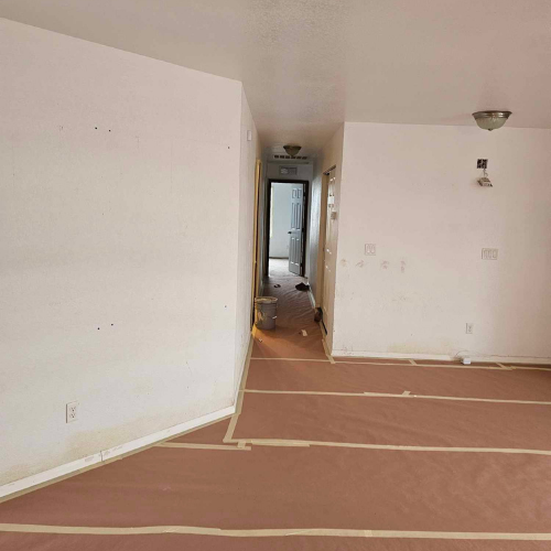 Renovated interior: White walls, brown paper floor covering, hallway leading to a door.
