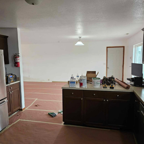 Kitchen renovation in progress: brown cabinets, red fire extinguisher, paint cans, and exposed flooring.