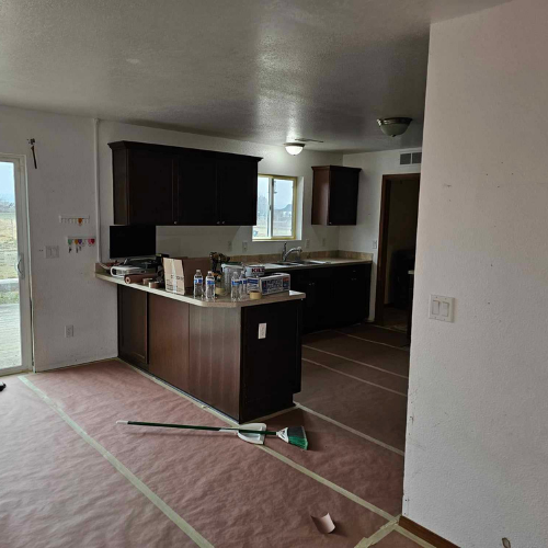 Kitchen with dark cabinets, countertop, island, window, and a door, in a house under construction.