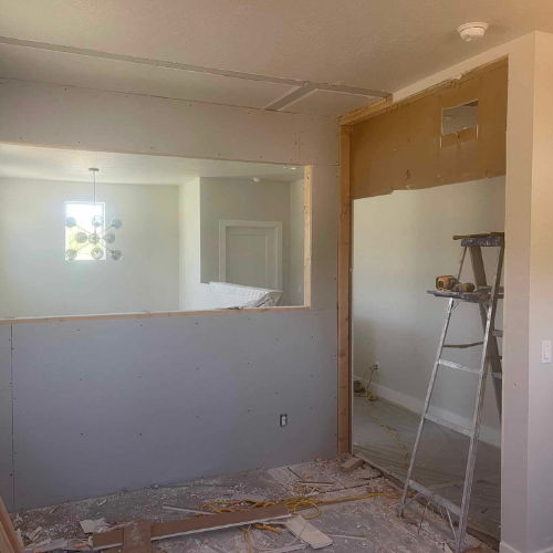 Room under construction, with drywall, ladder, and a doorway opening into another room.