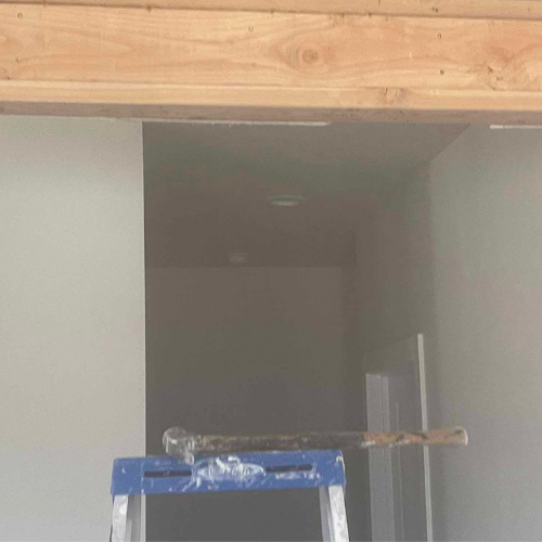 Interior construction site with wooden beam, gray walls, ladder, and tools.