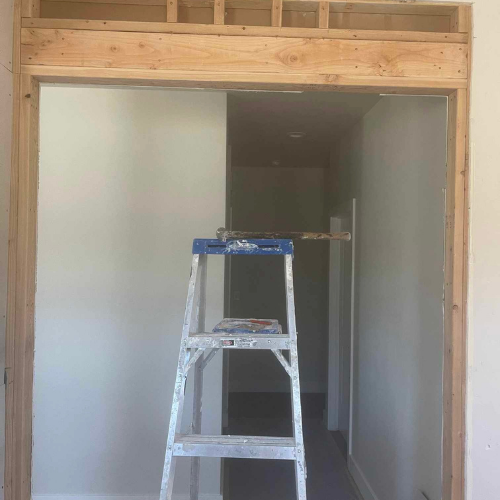 Wooden door frame under construction with a ladder inside, leading to a hallway.