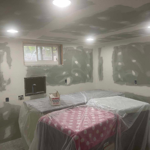 Room under construction, drywall patched. Two tables covered in plastic, one with pink polka dots.