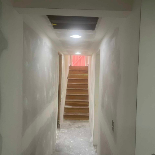 Hallway with stairs and an open ceiling access point. White walls and wooden stairs.