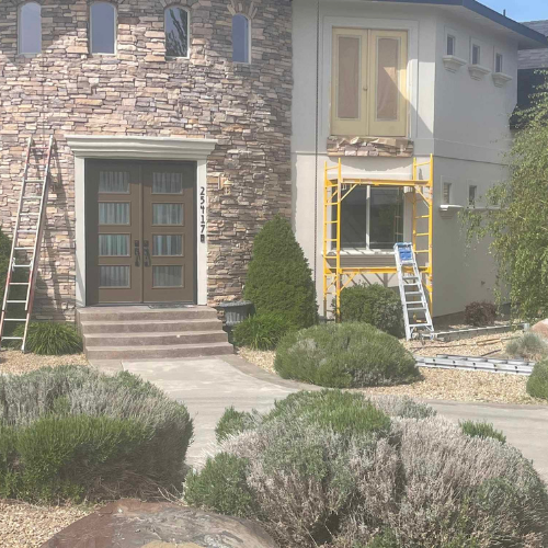 House exterior with stone facade and paint work in progress; ladders and scaffolding visible.