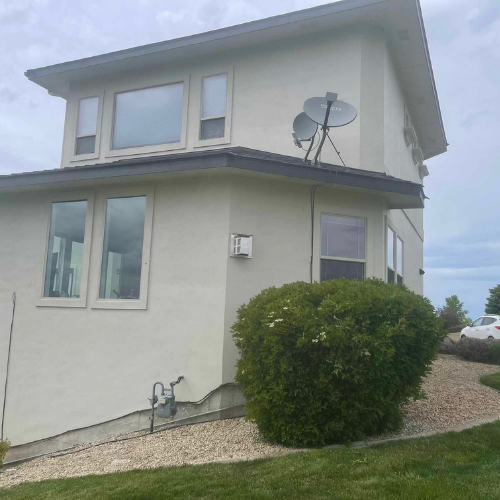 Two-story beige house with a shrub and satellite dishes on the roof.