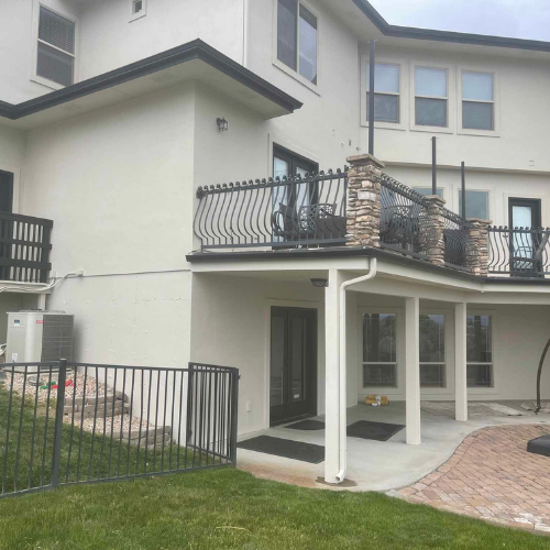 Back of a two-story beige house with black railings and a covered patio area.