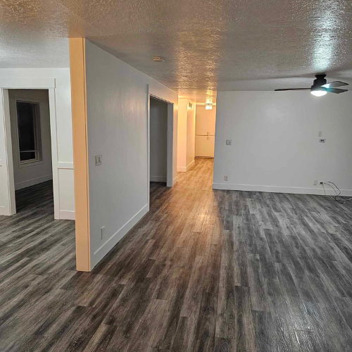 Interior view of a renovated home with gray wood flooring and white walls, featuring multiple doorways.