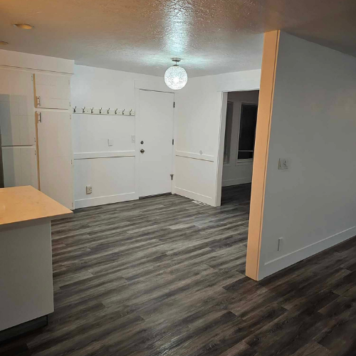 Open-concept kitchen and dining area with white cabinets, dark wood-look flooring, and a globe light fixture.