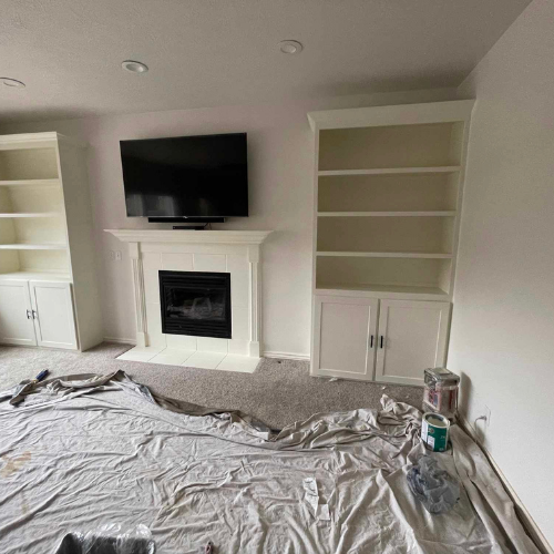 Living room with fireplace, built-in bookshelves, and TV. Painting in progress; drop cloth and paint cans on the floor.