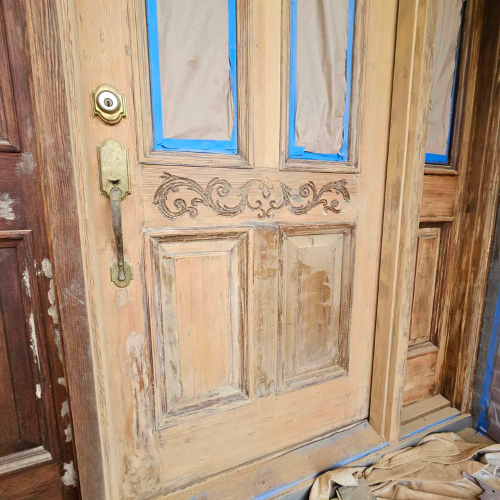 Wooden door being prepped for painting; blue tape surrounds window panes.