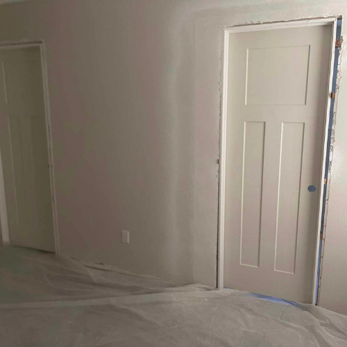 Interior view of a room with two white doors and a partially painted wall, covered floor.