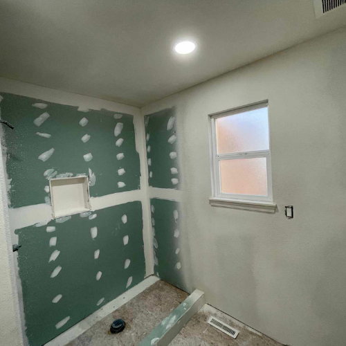 Bathroom under construction; green drywall, white walls, small window, unfinished floor.
