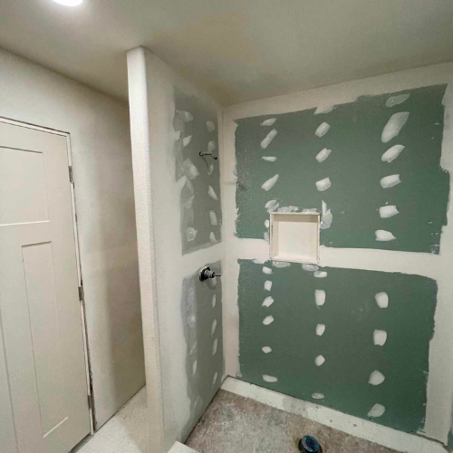 Bathroom under construction with green drywall, white door, and recessed shelf.