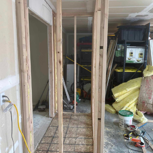 Interior framing with studs forming doorway. Wire mesh on floor. Garage interior in background.