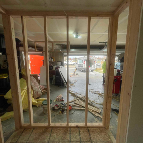 Wooden wall framing for a doorway, leading to a cluttered garage and the outdoors.