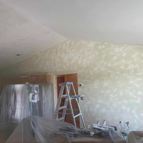 Interior wall with textured finish, ladder, and covered furniture; room under renovation, neutral tones.