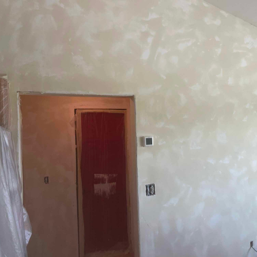 Interior view of a wall and door with a textured, light-colored paint finish. There's an open door and electrical fixtures.