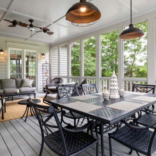 Screened porch with dining table and seating, lit by pendant lights and a ceiling fan, with a view of greenery outside.