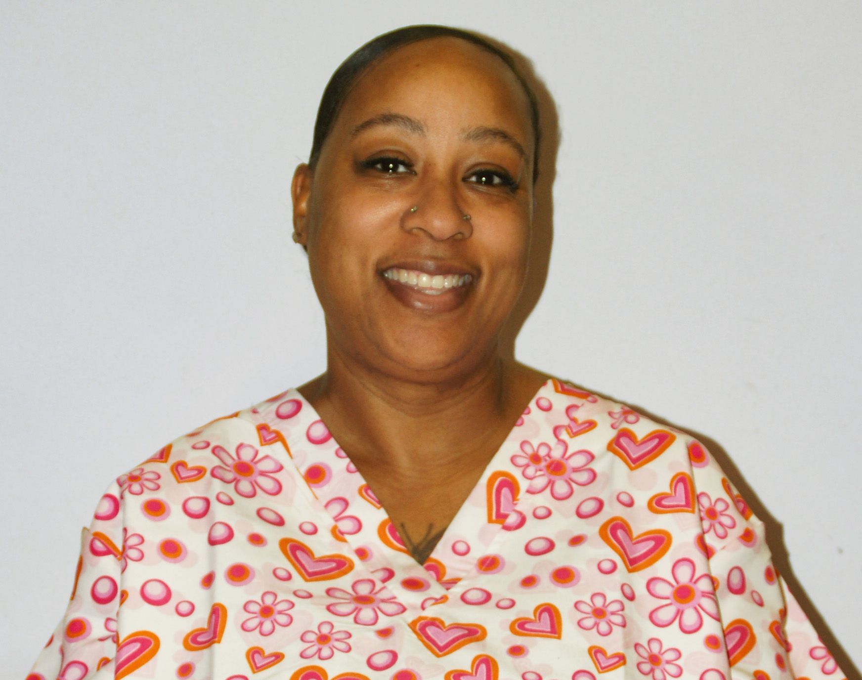 A woman wearing a pink shirt and a gold necklace is smiling for the camera.
