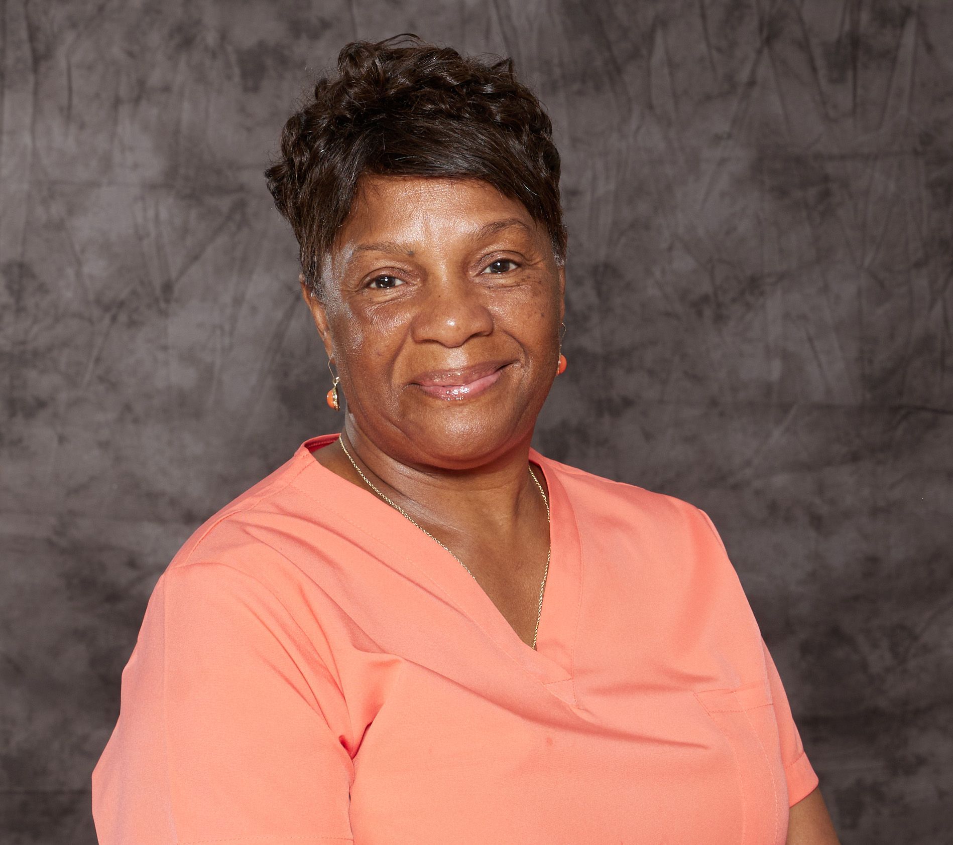A woman wearing a pink striped shirt and earrings is smiling for the camera.