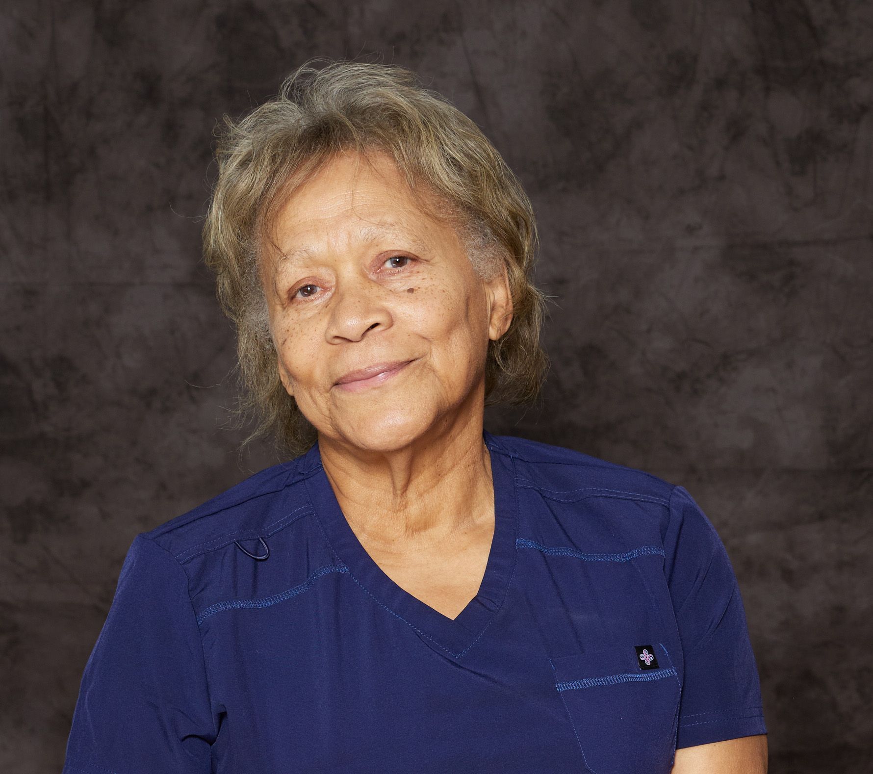 A woman in a blue shirt and gray sweater is smiling for the camera.