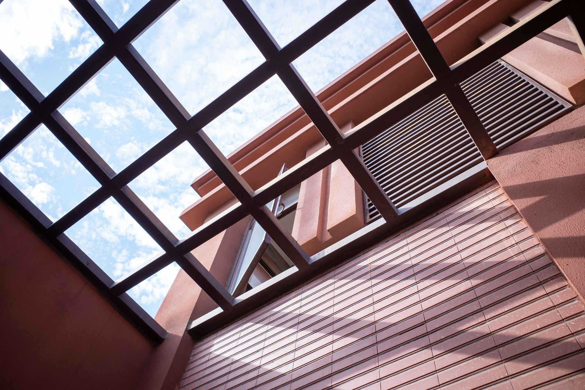 Brown wooden lattice roof over a light-colored building with blue sky peeking through the roof.