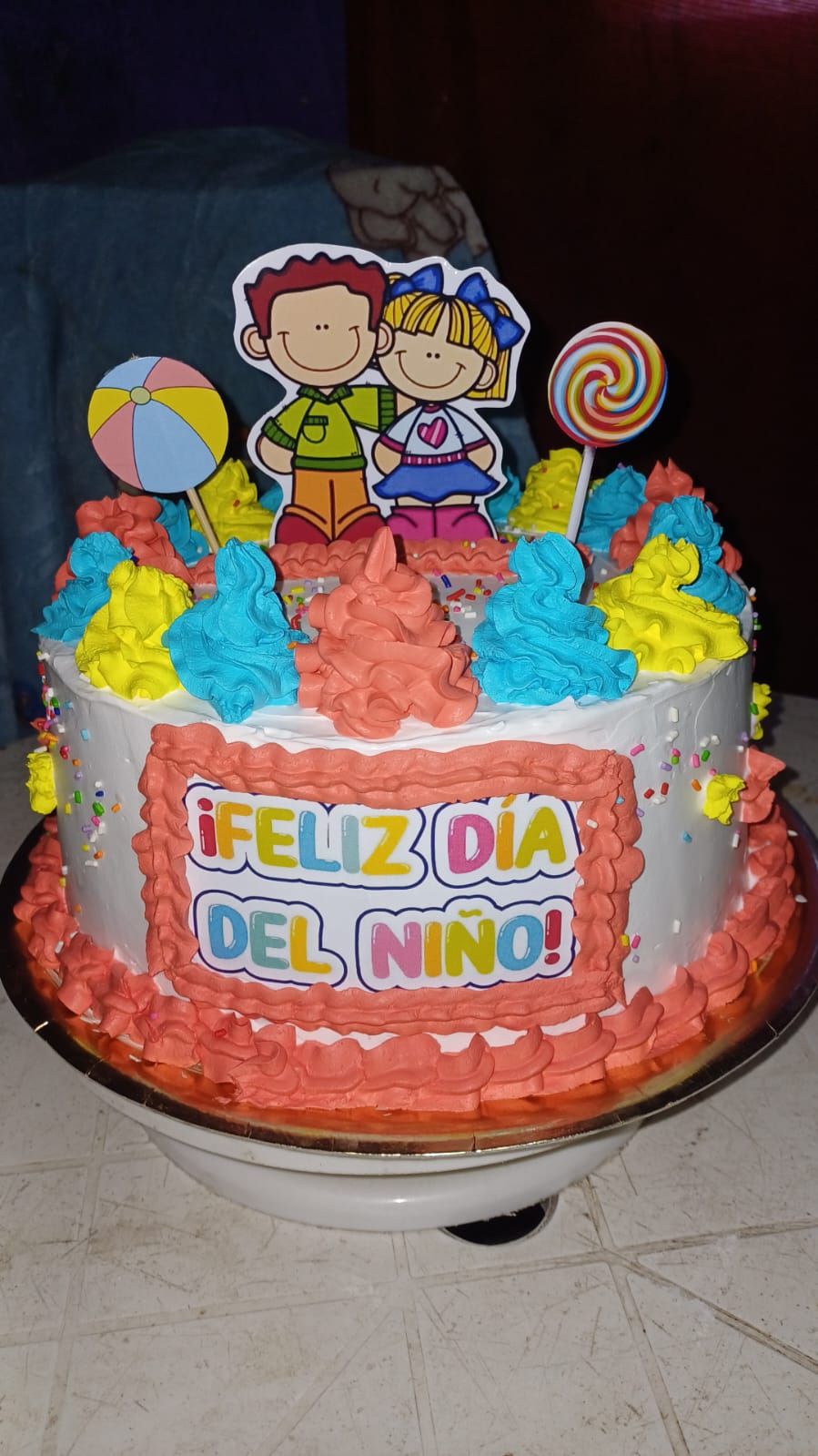 Pastel decorado para el Día del Niño. Tiene glaseado colorido, adornos de dibujos animados y el texto 