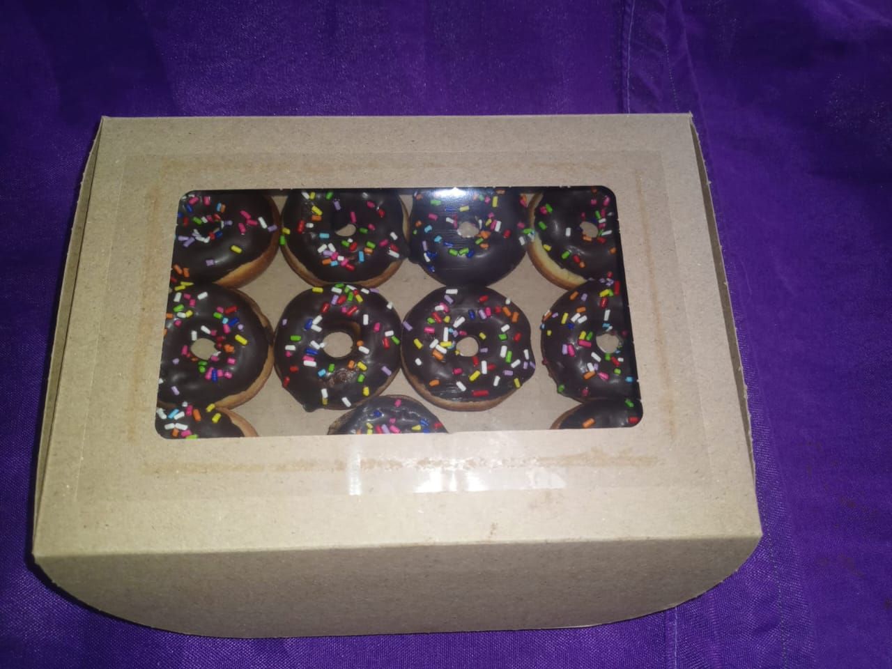 Caja de donas de chocolate con chispas, visible a través de una ventana.