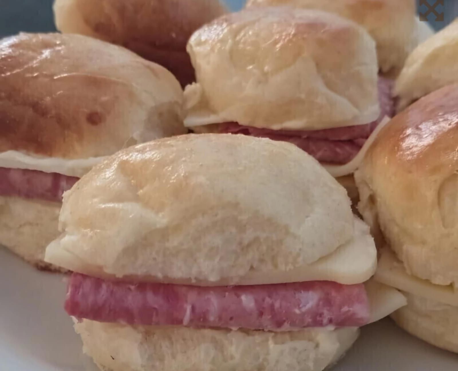 Mini sándwiches en un plato: suaves panecillos blancos con un visible relleno de carne rosada.
