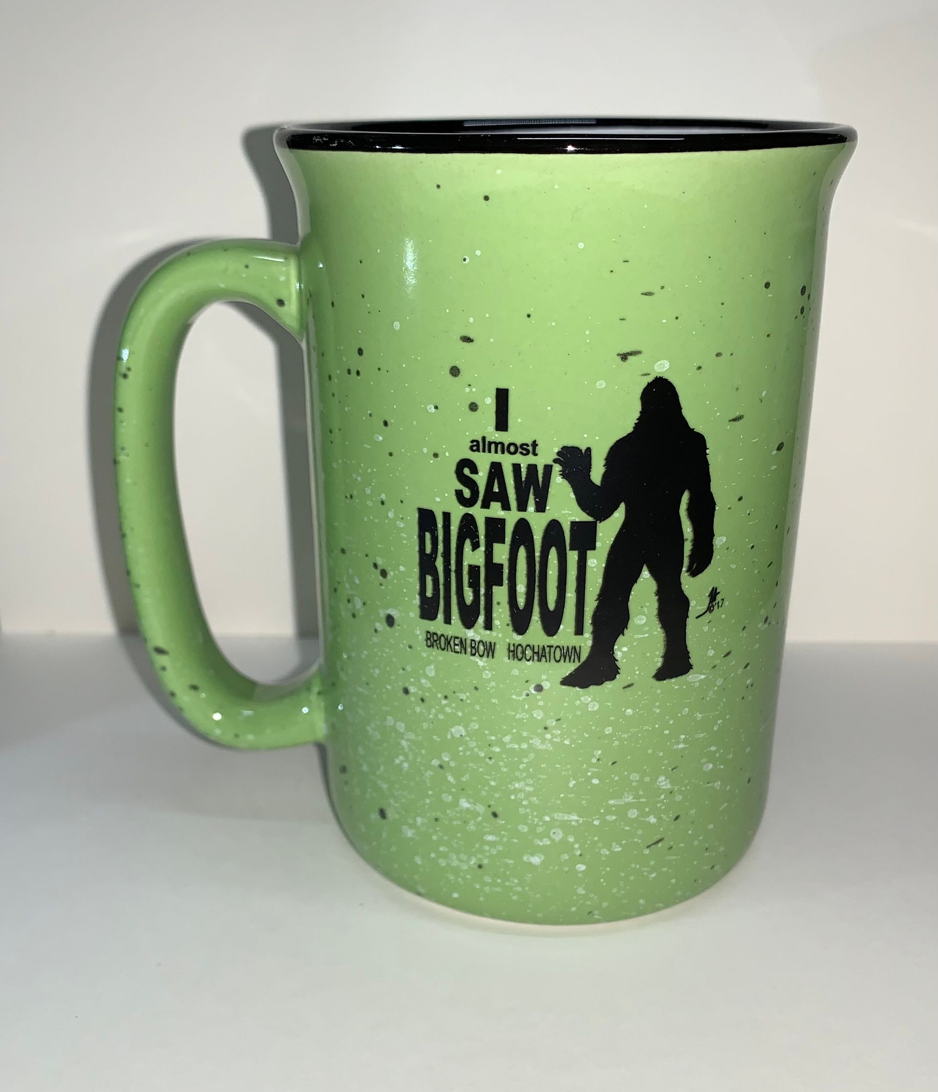 Green mug with black rim and Bigfoot silhouette text on a light background