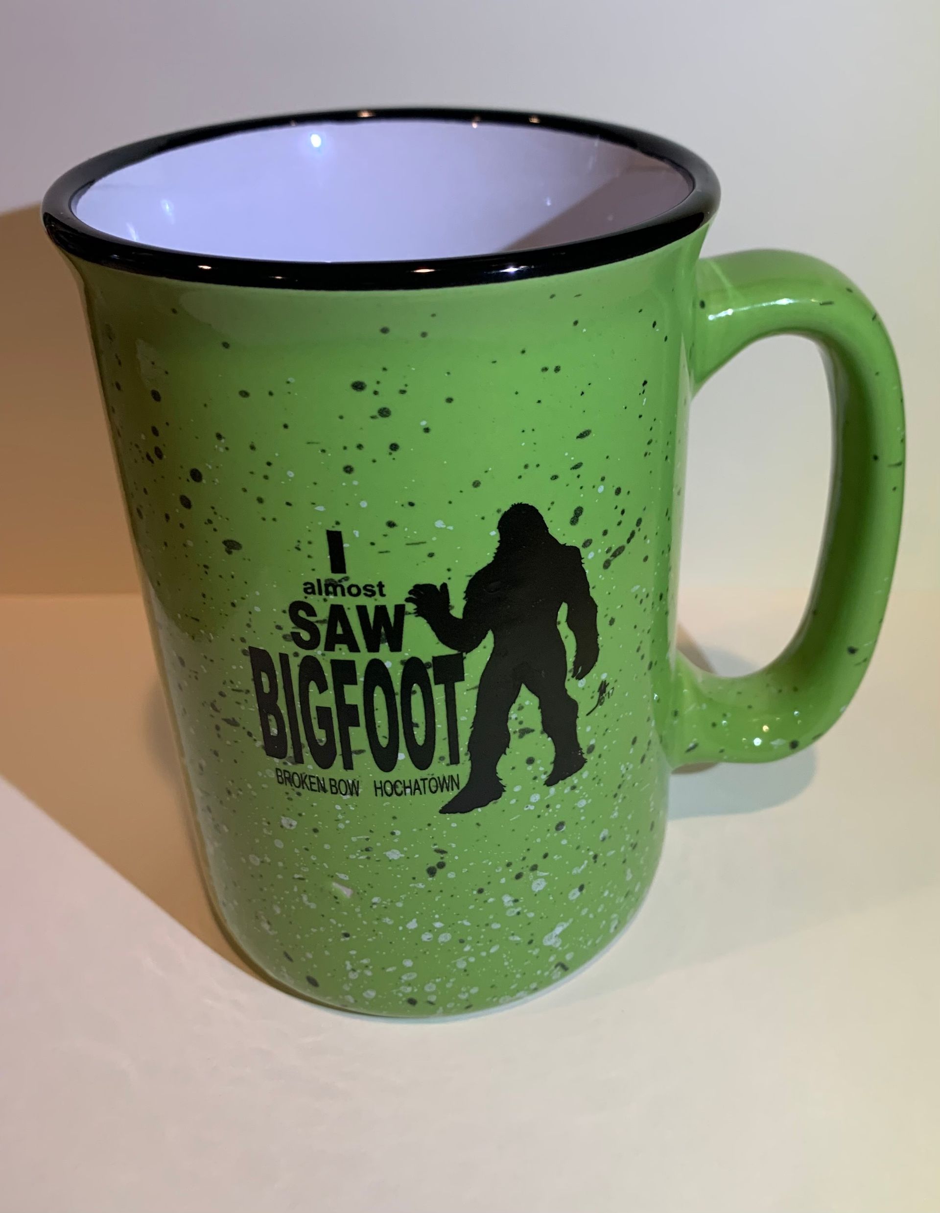 Green mug with black rim and Bigfoot silhouette text on a light background