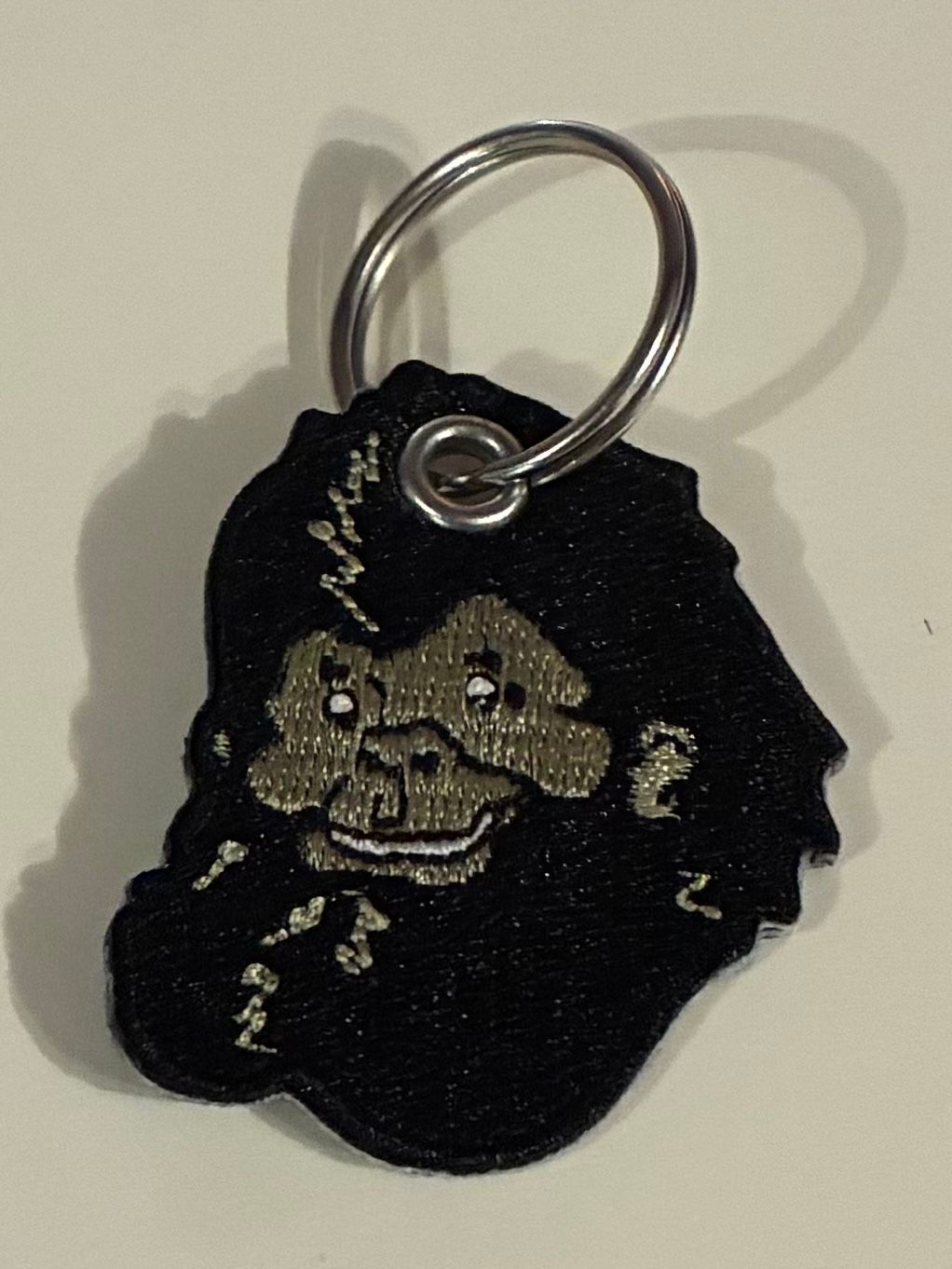 Black keychain tag with a cartoon face and metal ring on a light background