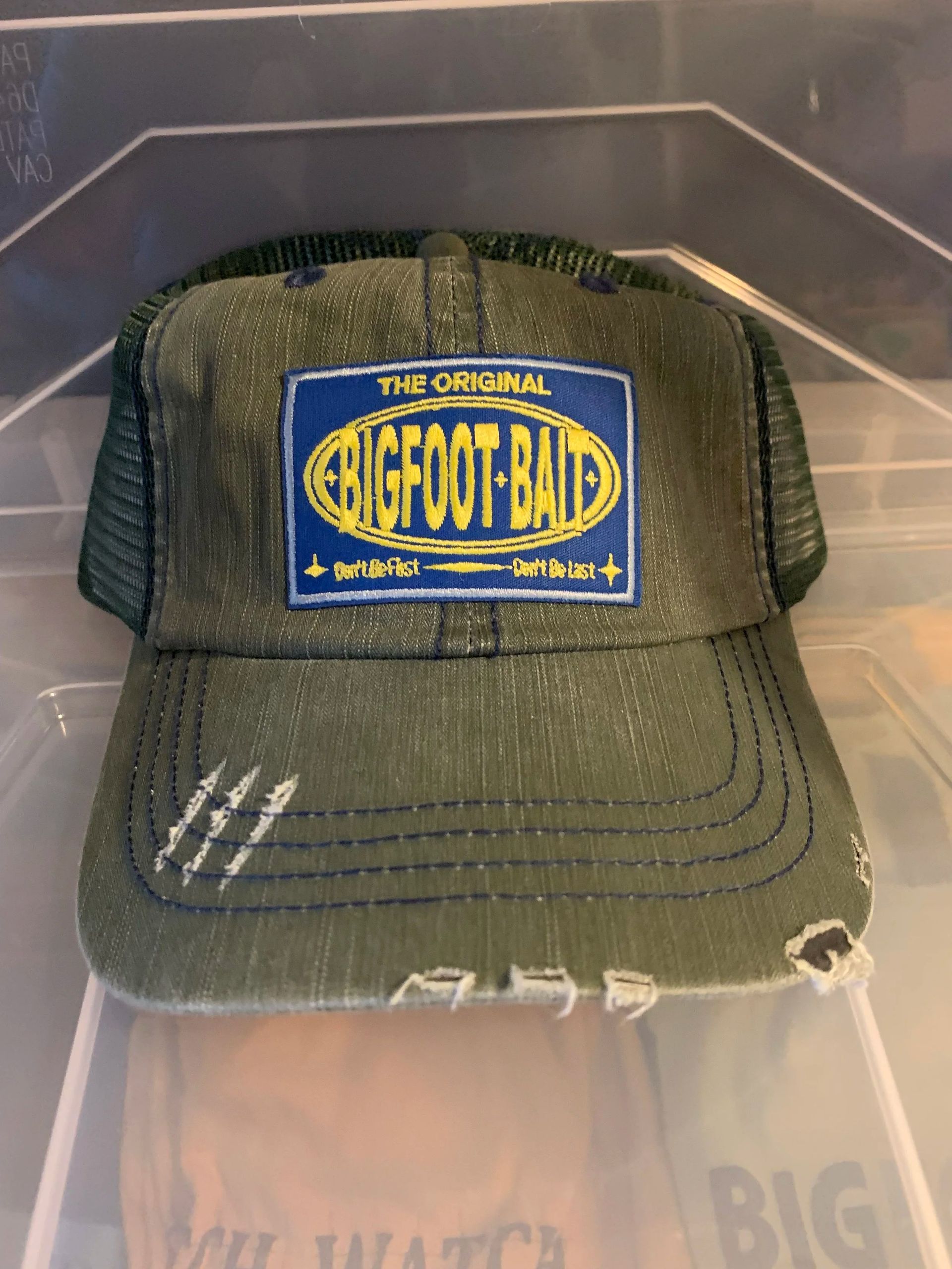 Worn green mesh trucker cap with blue-and-yellow “Jeff’s Bait” patch on a display shelf