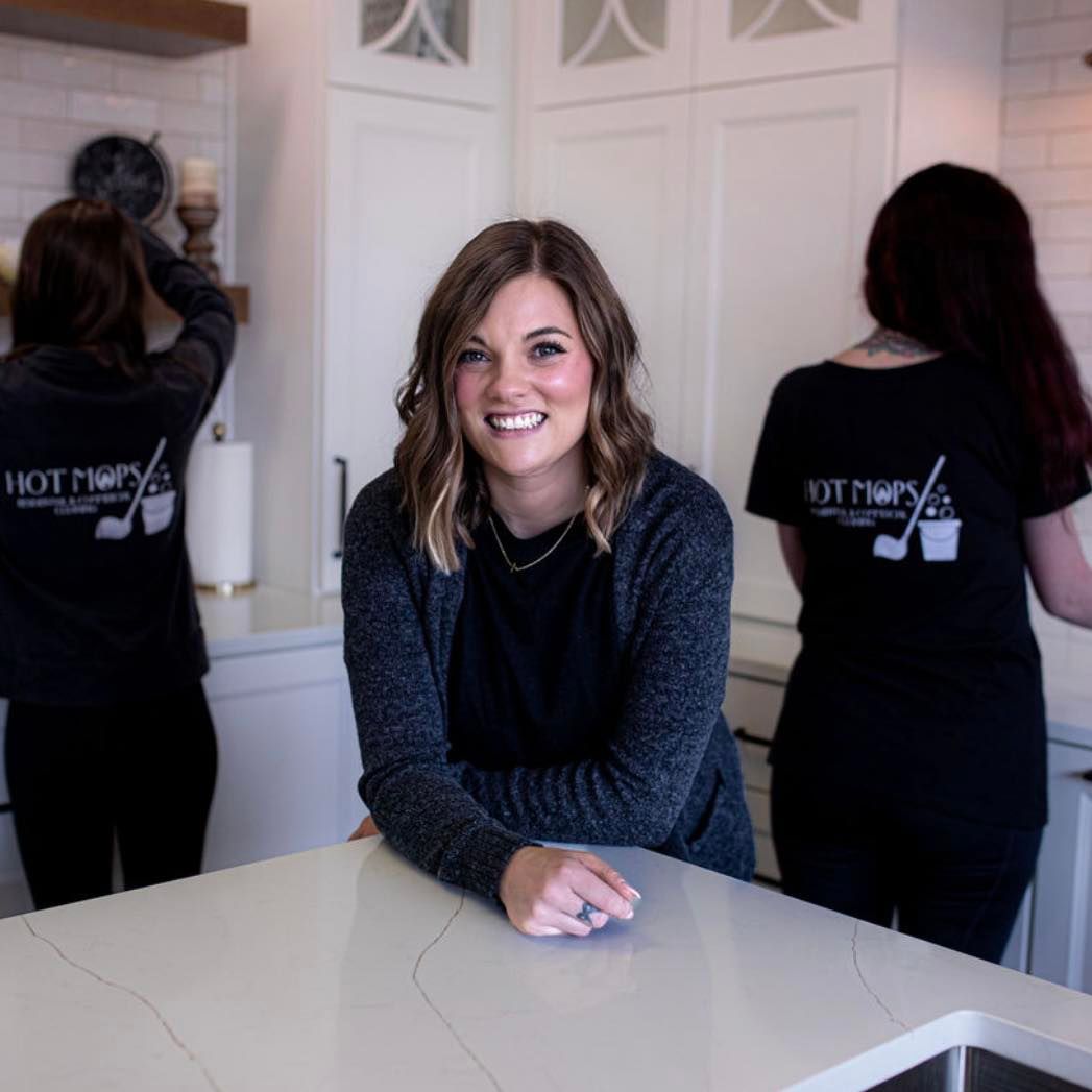 Woman smiling, leaning on kitchen counter, two others wearing
