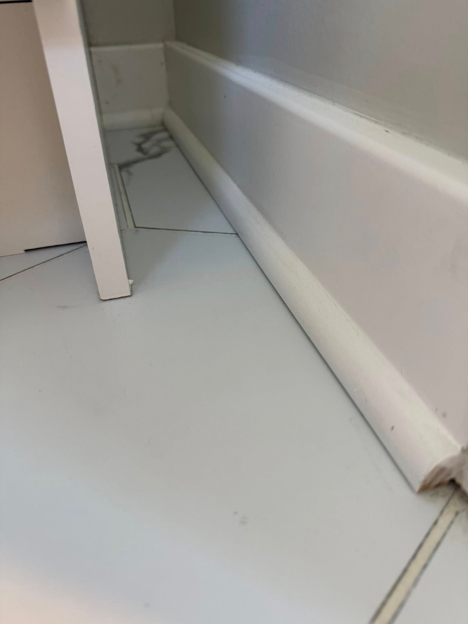 White baseboard trim meets white tiled floor. A cabinet leg is at the left.