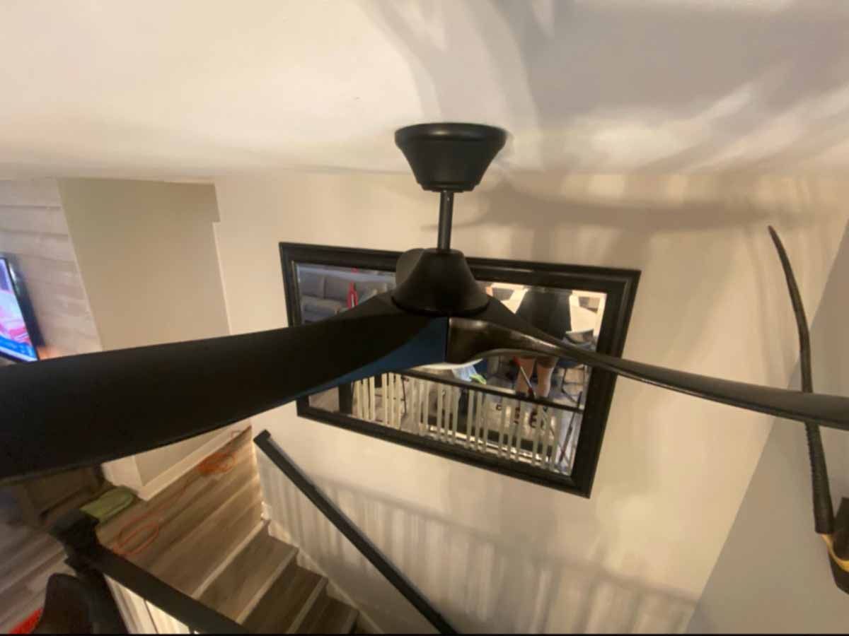 Black ceiling fan above a staircase, set against a white wall with a framed mirror.