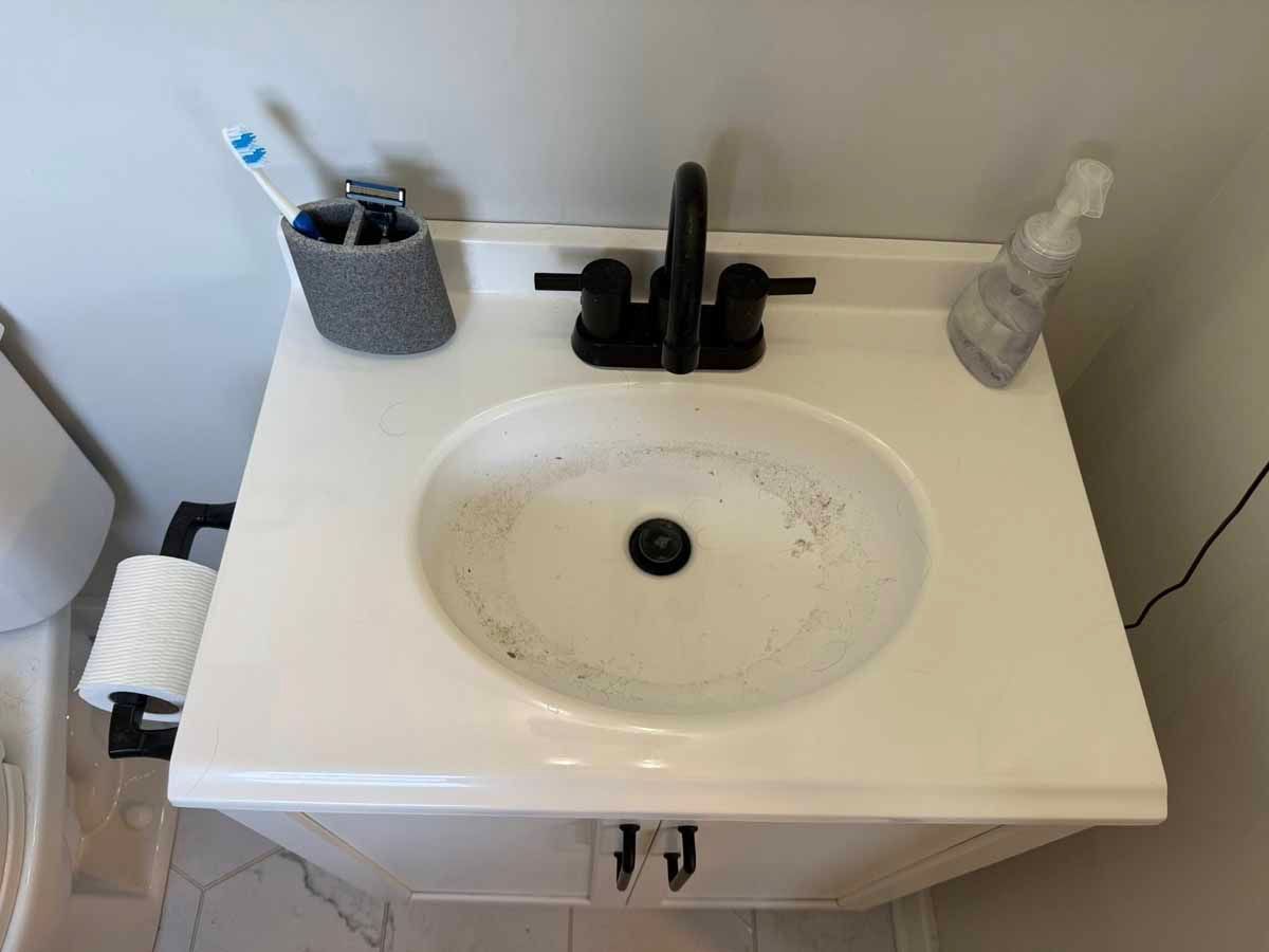 White bathroom sink with black faucet, toothbrush holder, and spray bottle on the countertop.