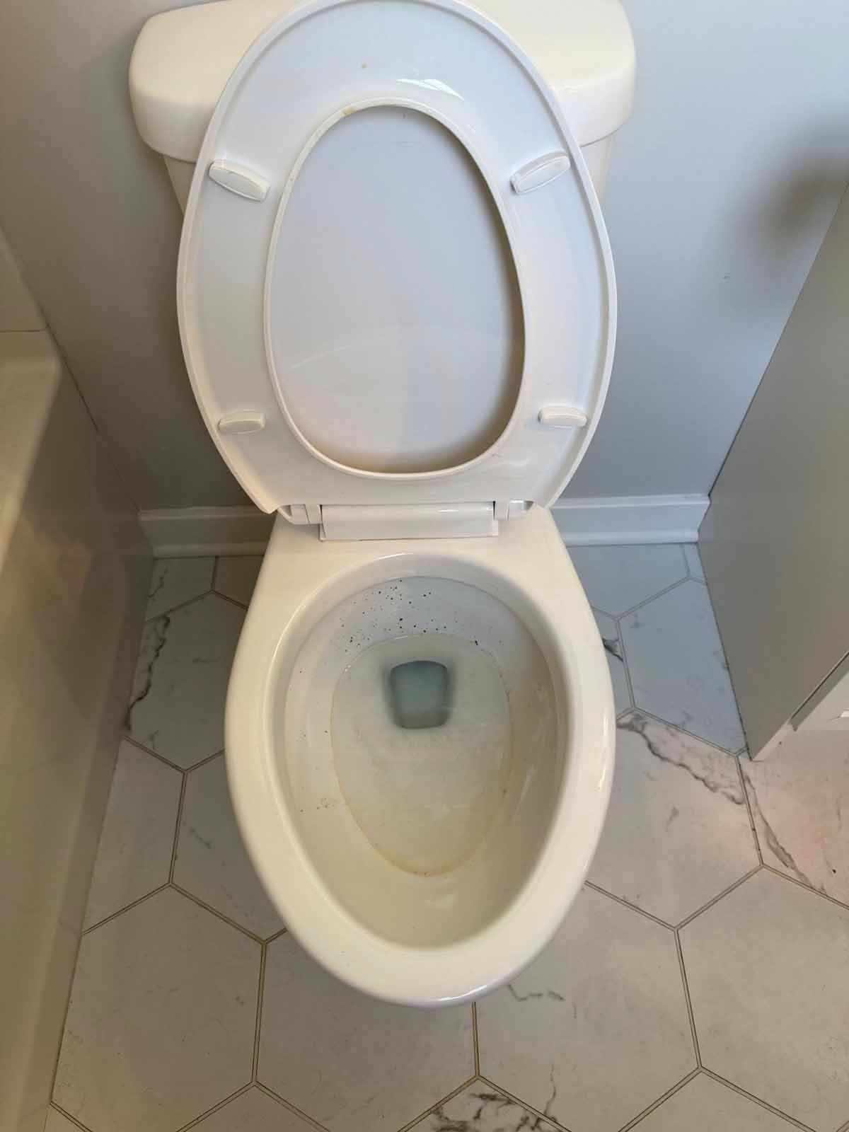 Top-down view of a white toilet with the seat up, on light gray and white patterned hexagonal floor tiles.