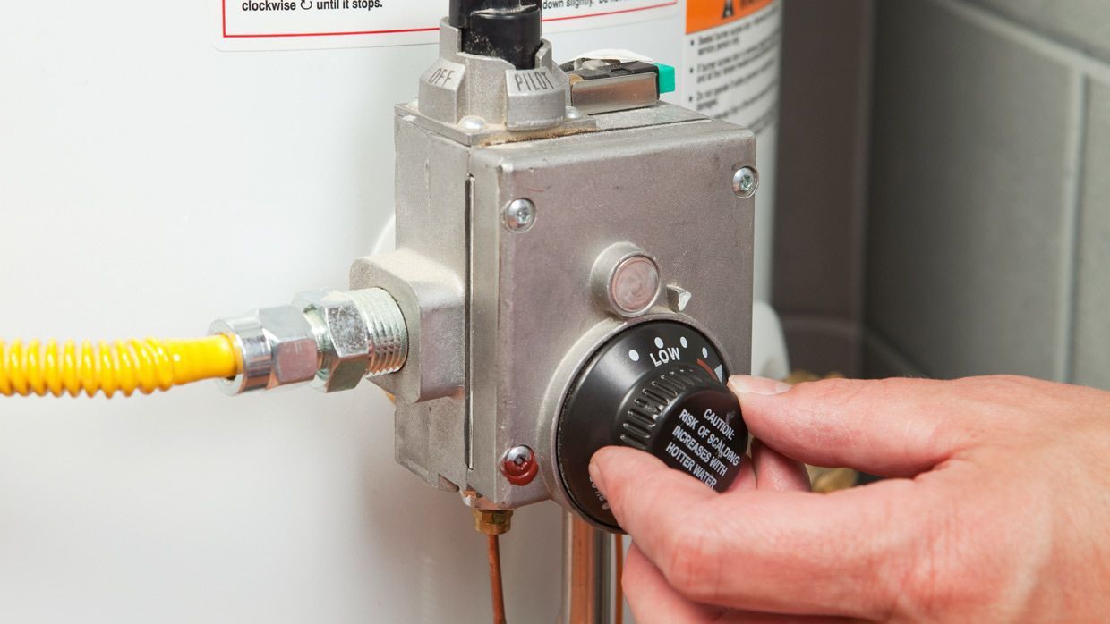 a person is adjusting the temperature of a gas water heater .