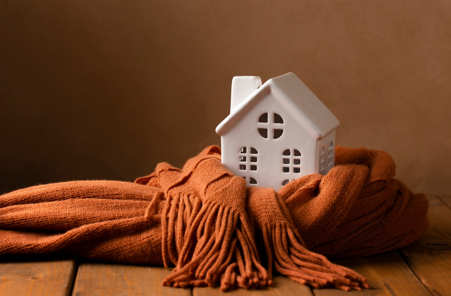 A small white house wrapped in a scarf on a wooden table