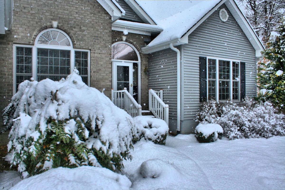 Snow-covered house with gray siding, arched windows, and snow-laden bushes.