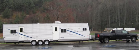A caravan is parked in a grassy field next to a body of water.